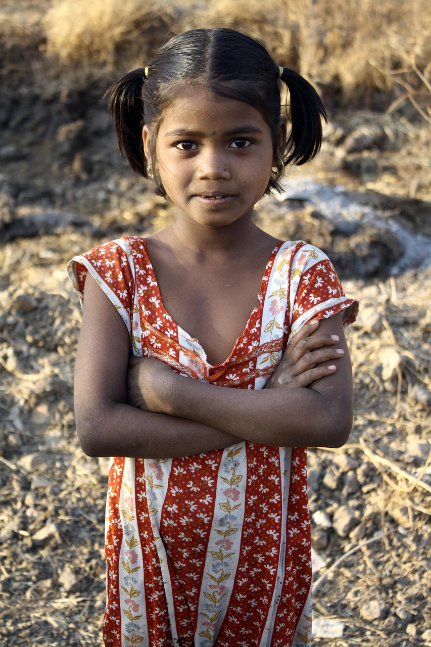 Young girl in a red patterned dress standing confidently outdoors
